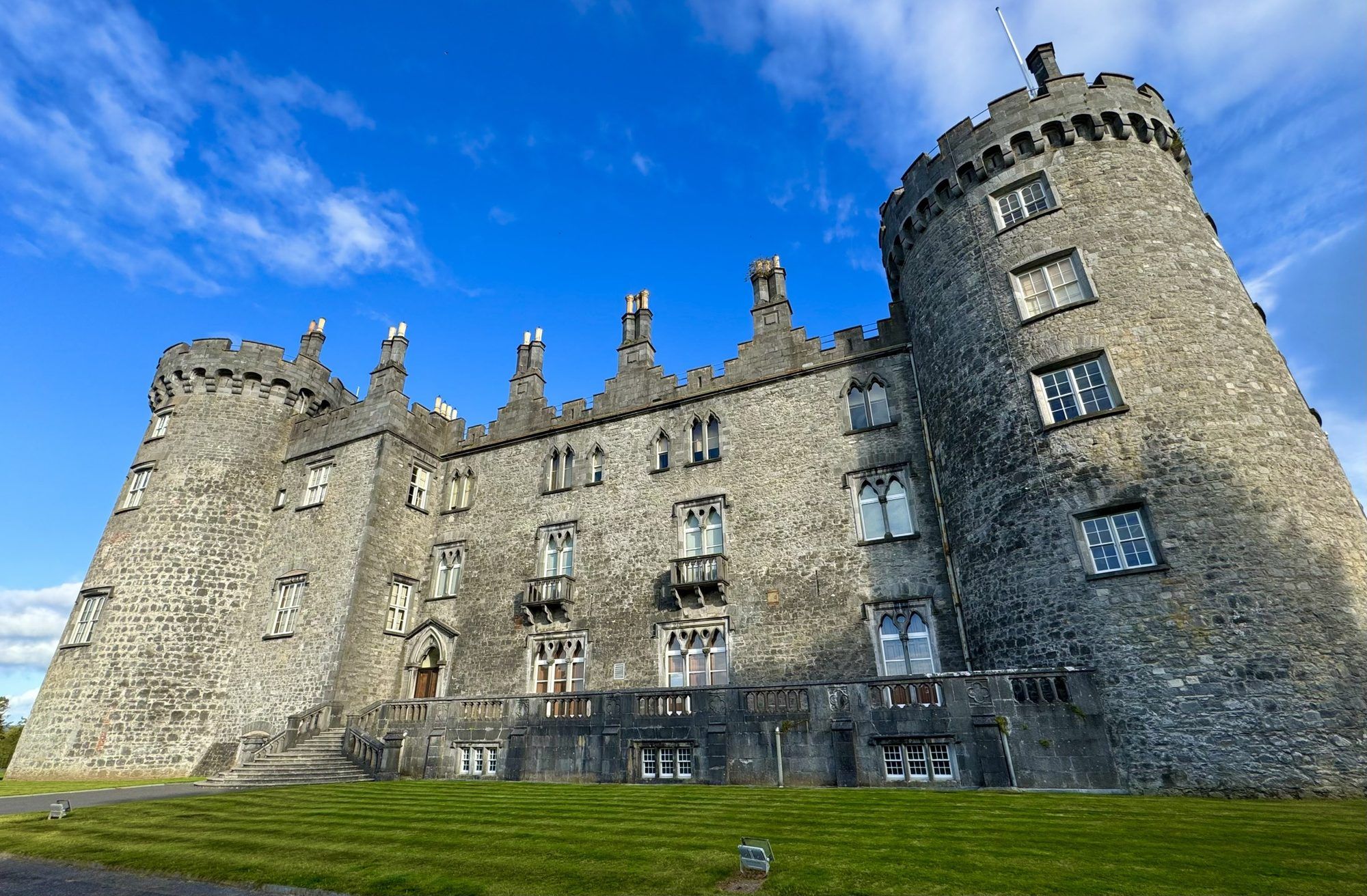 The towers and limestone walls of Kilkenny Castle against a blue sky
