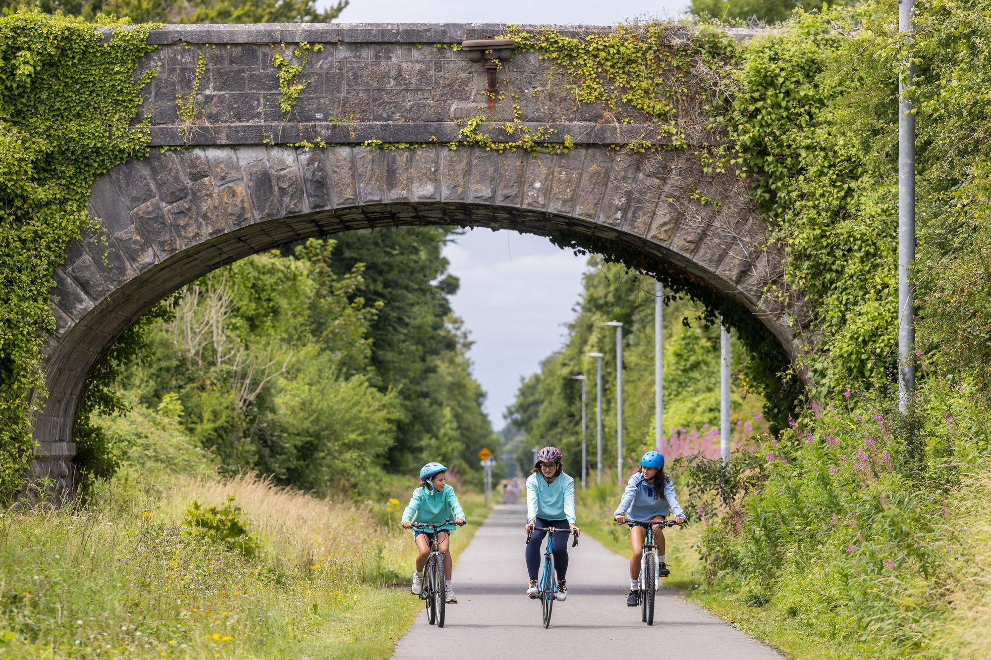 Cyclists passing under a stone bridge on the Old Rail Trail Greenway